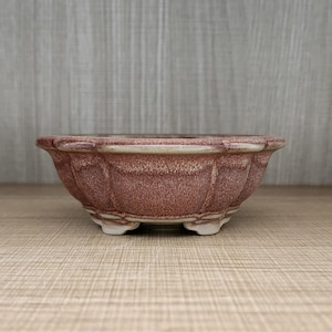 Op de afbeelding: Een roodbruine keramische bonsai pot met een geschulpte rand en kleine voetjes. De pot heeft een textuur en een lichtgekleurde rand. Deze decoratieve container is ontworpen voor kleine planten en voegt elegantie toe.