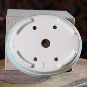May include: A light blue oval ceramic bonsai pot with four drainage holes and a square mark on the bottom.
