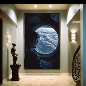 Puede incluir: Una gran impresión enmarcada de un astronauta mirando la Tierra a través de una ventana circular de una nave espacial. La obra de arte, en tonos azules y negros, crea una escena dramática. La impresión se exhibe en un pasillo.