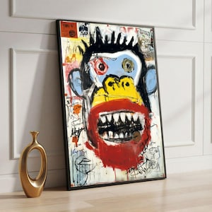 May include: Abstract monkey portrait art print in a black frame. The artwork features a monkey face with a blue face, yellow mouth, red lips, and black teeth. The background is white with colorful graffiti-style markings. A gold vase is in the foreground.