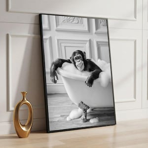 May include: Black and white framed print of a chimpanzee relaxing in a claw-foot bathtub filled with bubbles. The chimpanzee is smiling and appears to be enjoying the bath. A gold vase is in the foreground.