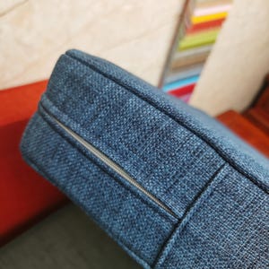 May include: Close-up of a blue cushion with a zipper running along the side. The cushion is made of a textured fabric.