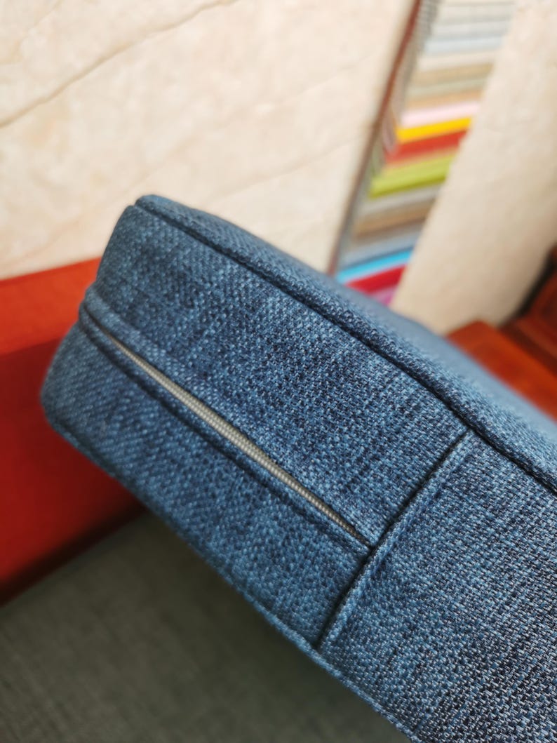 May include: Close-up of a blue cushion with a zipper running along the side. The cushion is made of a textured fabric.