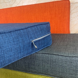 May include: Three cushions stacked on top of each other. The top cushion is blue, the middle cushion is gray, and the bottom cushion is green. The blue cushion has a zipper.