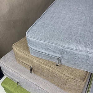 Puede incluir: Una pila de cuatro cojines rectangulares de diferentes colores. El coj&iacute;n superior es gris claro, el segundo es beige, el tercero es gris claro y el inferior es verde. Cada coj&iacute;n tiene una cremallera en el lateral.