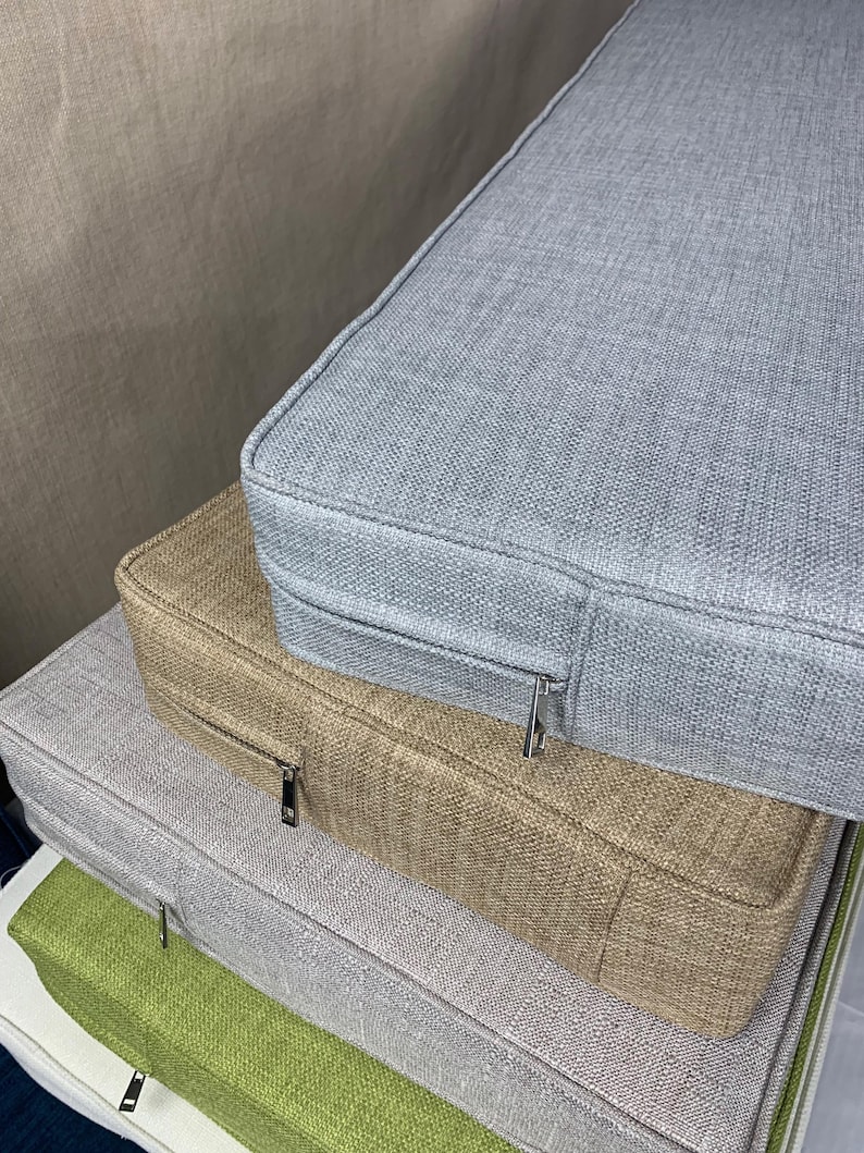Puede incluir: Una pila de cuatro cojines rectangulares de diferentes colores. El coj&iacute;n superior es gris claro, el segundo es beige, el tercero es gris claro y el inferior es verde. Cada coj&iacute;n tiene una cremallera en el lateral.