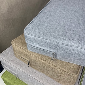 May include: Four stackable cushion covers in different colors and textures. The top cushion is light gray, the second is beige, the third is light gray, and the bottom is green. All cushions have zippers.