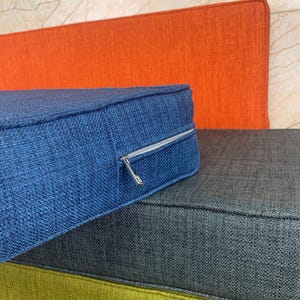 Puede incluir: Un conjunto de tres cojines de diferentes colores. El coj&iacute;n superior es azul con una cremallera, el coj&iacute;n del medio es gris y el coj&iacute;n inferior es verde.