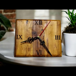 May include: A wooden clock with Roman numeral markings on a square wooden base. The clock has black hands and a red second hand.