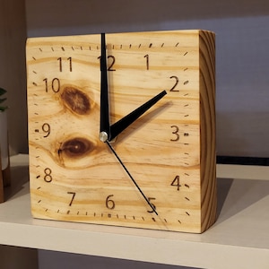 Puede incluir: Un reloj de madera con agujas negras y números romanos. El reloj está hecho de madera clara con un patrón de veta natural.