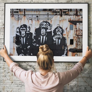 May include: Black and white graphic print of three monkeys wearing suits and ties. The monkeys are in front of a weathered, industrial background. The text "Like the Lancaster" is visible in the background.