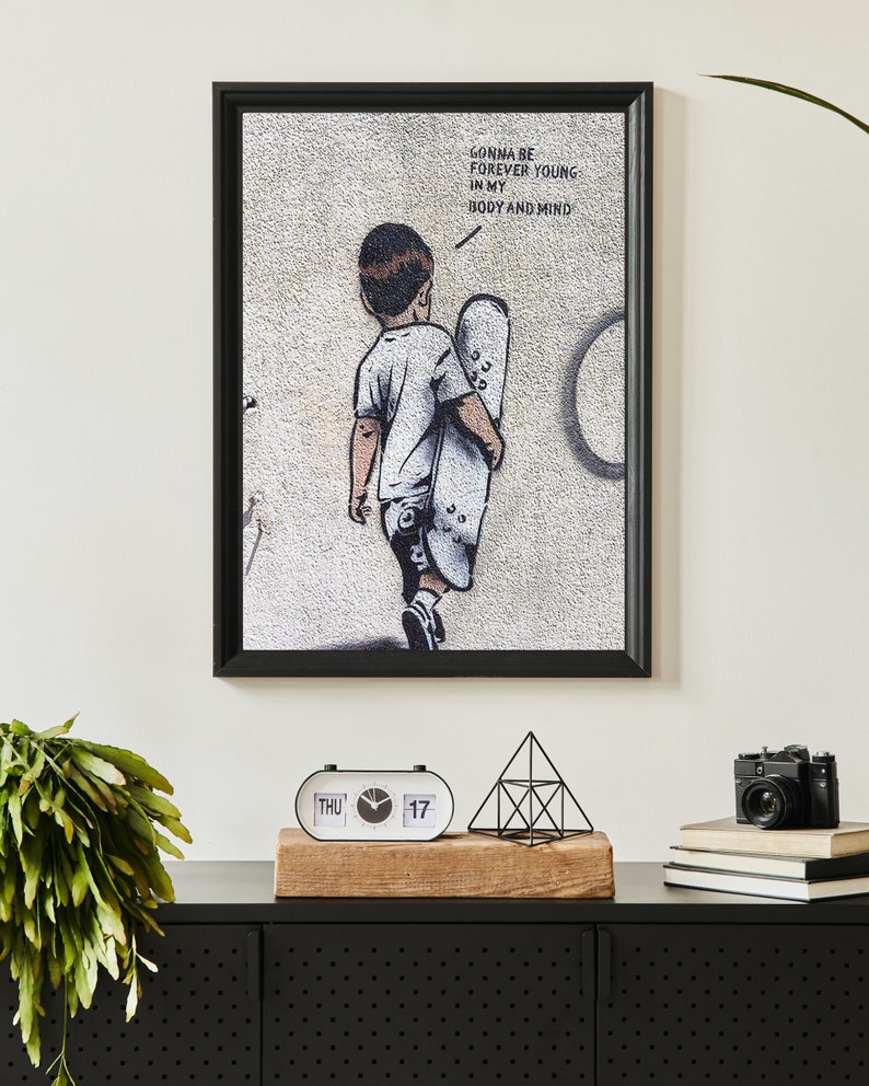 Pu&ograve; includere: Stampa incorniciata in bianco e nero di un bambino che tiene uno skateboard con il testo "Gonna be forever young in my body and mind".