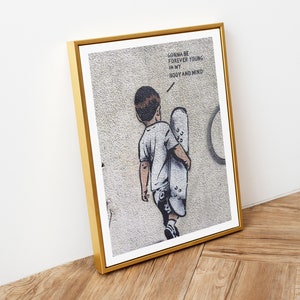 Pu&ograve; includere: Una stampa incorniciata di un'opera d'arte graffiti in bianco e nero che raffigura un giovane che tiene uno skateboard. Il testo sul muro dice "Gonna be forever young in my body and mind."