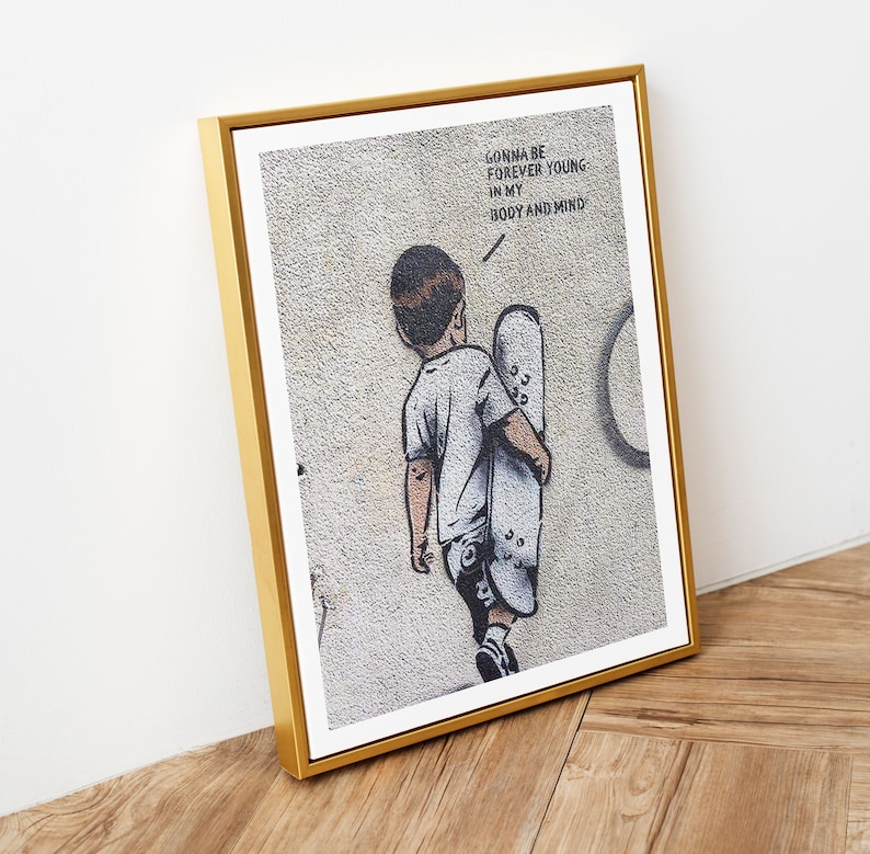 Pu&ograve; includere: Una stampa incorniciata di un'opera d'arte graffiti in bianco e nero che raffigura un giovane che tiene uno skateboard. Il testo sul muro dice "Gonna be forever young in my body and mind."