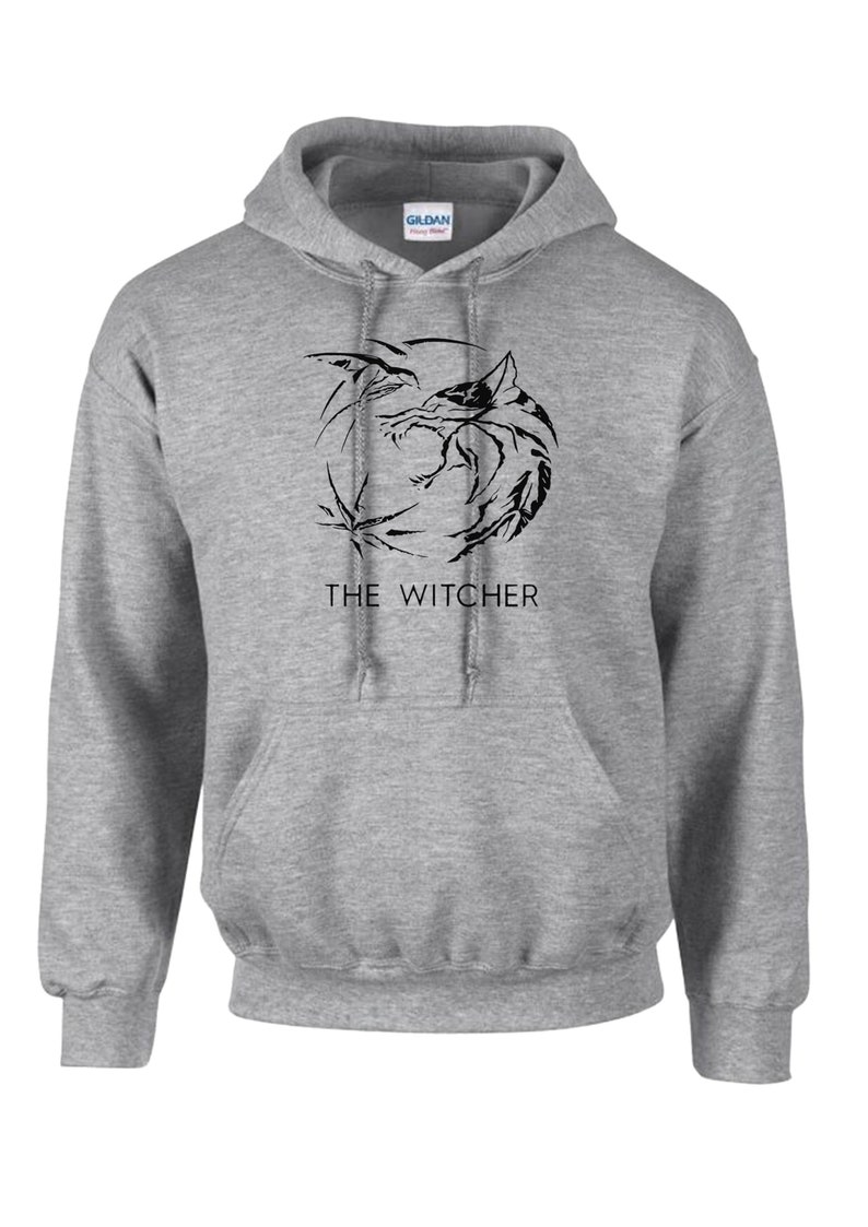 K&ouml;nnte beinhalten: Ein grauer Kapuzenpullover mit einem schwarzen Aufdruck eines Wolfskopfes und dem Text "THE WITCHER" auf der Vorderseite.