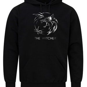 K&ouml;nnte beinhalten: Schwarzer Kapuzenpullover mit einem silbernen Aufdruck des Witcher-Logos und dem Text "THE WITCHER" darunter.