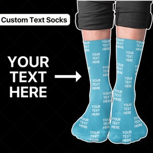 Könnte beinhalten: Hellblaue Socken mit den Worten "YOUR TEXT HERE" in Weiß wiederholt. Die Socken werden auf den Beinen einer Person vor einem schwarzen Hintergrund gezeigt. Oben links steht "Custom Text Socks".