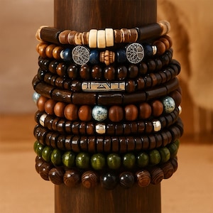 May include: A stack of wooden beaded bracelets in various shades of brown, green, and cream. Some bracelets feature silver accents and decorative charms. The bracelets are displayed on a wooden cylinder.