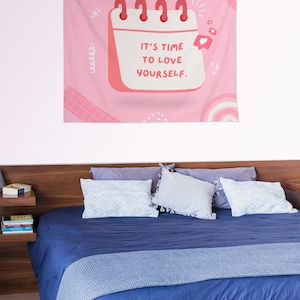 May include: Pink tapestry with a calendar design that says "It's time to love yourself." The calendar has a pink background and white text. There are also pink and white clouds, hearts, and stars on the tapestry.