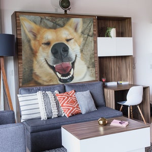 May include: A gray couch with pillows in a living room setting. The couch has a tapestry hanging above it featuring a close-up of a dog's face with its mouth open and tongue sticking out.