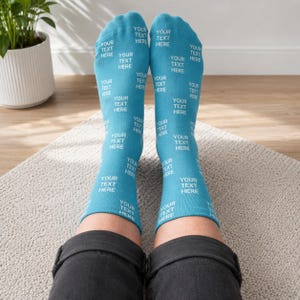 May include: A pair of light blue crew socks featuring a repeating pattern of the white text "YOUR TEXT HERE" printed across the entire surface. The socks are made of a soft fabric and extend to the mid-calf, providing a consistent look on both feet.