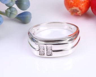 Puede incluir: Un anillo de banda de plata con dos pequeños diamantes engastados en el centro. El anillo tiene un acabado liso y pulido.