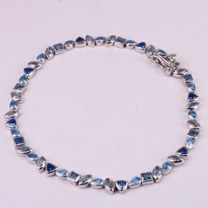 May include: A silver bracelet with blue gemstones of various shapes and sizes. The bracelet has a clasp closure.