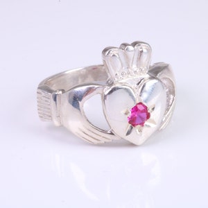 Peut inclure: Bague Claddagh en argent avec un cœur orné d'une pierre rouge, une couronne et des mains jointes. Ce bijou symbolise l'amour, la loyauté et l'amitié. Un bijou classique.