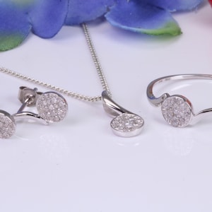 May include: A silver jewelry set with a necklace, earrings, and a ring. Each piece features a small, round, pave-set diamond pendant.