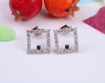 May include: A pair of silver square stud earrings with a small black stone in the center of each square. The earrings are surrounded by clear cubic zirconia stones.