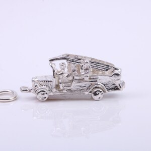 Op de afbeelding: Zilveren bedel van een vintage brandweerwagen met een ladder en twee figuren in de cabine. De bedel heeft een lus om aan een armband of ketting te bevestigen.