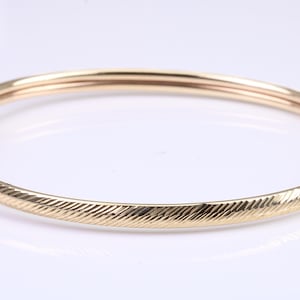 May include: A gold bangle bracelet with a textured design. The bracelet is made of a single piece of metal and has a simple, elegant design.