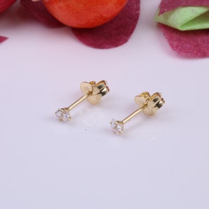 May include: A pair of gold stud earrings with small, clear cubic zirconia stones.