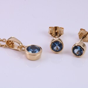 May include: A gold necklace and earrings set with a blue gemstone pendant and matching earrings.