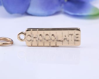 May include: A gold-toned metal charm shaped like a rectangular chocolate bar with the word CHOCOLATE embossed horizontally across the center. The charm features a small circular loop on the left side and is accompanied by a separate gold-toned jump ring.