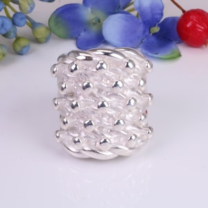 Puede incluir: Un anillo de plata con un diseño texturizado y tejido. El anillo está formado por pequeñas cuentas redondas que están conectadas por finos hilos de plata.