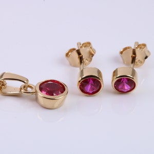 May include: A gold necklace and earrings set with a pink gemstone pendant and matching earrings.