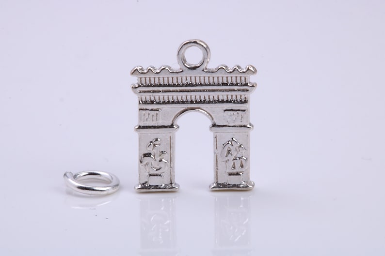 May include: Silver charm shaped like the Arc de Triomphe in Paris, France. The charm has a loop at the top for attaching to a bracelet or necklace.