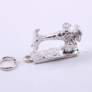 May include: A silver charm in the shape of a vintage sewing machine. The charm has a detailed design and a loop for attaching to a bracelet or necklace.