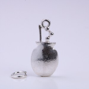 May include: Silver charm in the shape of a small pot with a single stem and a few beads on top. The charm has a textured surface and a loop for attaching to a bracelet or necklace.