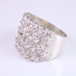 May include: A silver ring with a textured, organic design. The ring is wide and has a thick band.