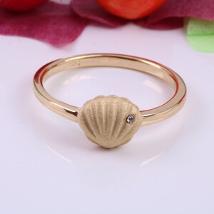May include: A gold ring with a textured seashell design and a small clear stone in the center.