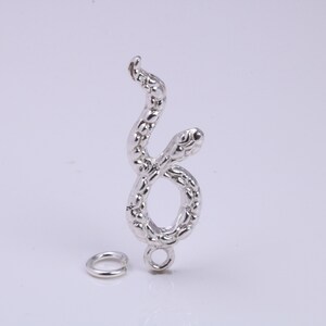 Puede incluir: Encanto de serpiente de plata con una superficie texturizada y un anillo de salto. La serpiente está enroscada en posición vertical.