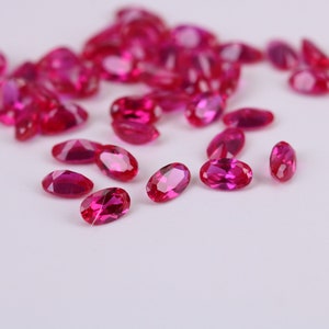 May include: A collection of oval-shaped, bright pink gemstones. The gemstones are scattered on a white surface.