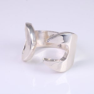 Puede incluir: Un anillo de plata con un diseño abstracto único. El anillo está abierto y tiene una forma curva.