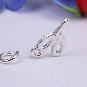 May include: Silver-toned metal charm shaped like a pair of scissors. The charm is attached to a silver-toned metal jump ring.