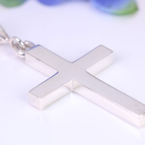 May include: A silver cross pendant with a simple design. The pendant has a smooth, polished finish and is attached to a bail.