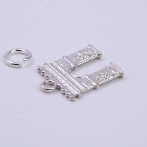 May include: Silver charm in the shape of an archway with detailed carvings. The charm has a jump ring attached for easy hanging.