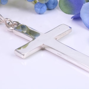 Op de afbeelding: Een zilveren kruis hanger met een eenvoudig ontwerp. De hanger heeft een gladde, gepolijste afwerking en een lus om aan een ketting te bevestigen.