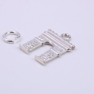 May include: Silver charm in the shape of the Arc de Triomphe, a famous Parisian landmark. The charm has a jump ring attached for easy attachment to a necklace or bracelet.